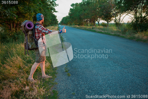 Image of Young caucasian tourist hitchhiking along a road.