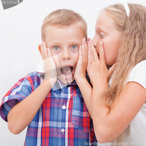 Image of Teenage girl whispering in the ear of a secret teen boys on white  background