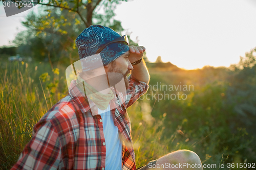 Image of Young caucasian man with backpack sitting on the top of hill