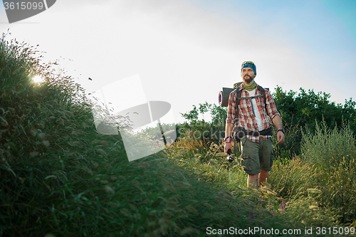 Image of Young caucasian man with backpack walking on a green meadow