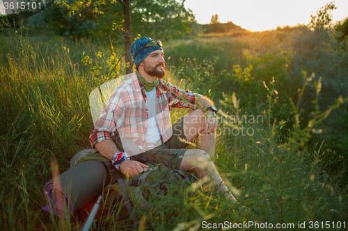 Image of Young caucasian man with backpack sitting on the top of hill