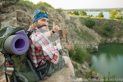 Image of Young caucasian man with backpack sitting on the top of hill