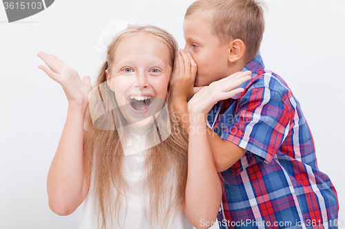 Image of Teenage boy whispering in the ear a secret to teen girl on white  background