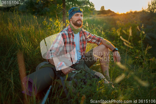 Image of Young caucasian man with backpack sitting on the top of hill