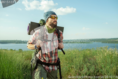 Image of Young caucasian man with backpack walking on the top of hill