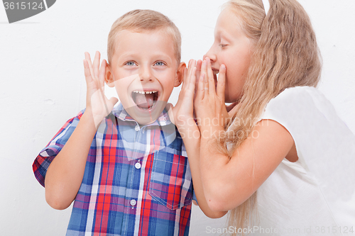 Image of Teenage girl whispering in the ear of a secret teen boys on white  background