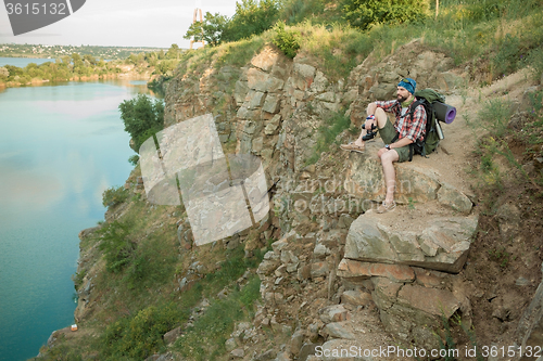 Image of Young caucasian man with backpack sitting on the top of hill