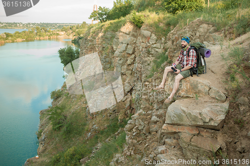 Image of Young caucasian man with backpack sitting on the top of hill