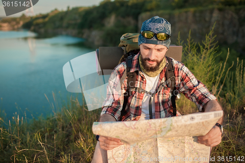Image of Young caucasian man with backpack sitting on the top of hill