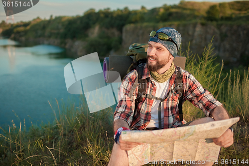 Image of Young caucasian man with backpack sitting on the top of hill