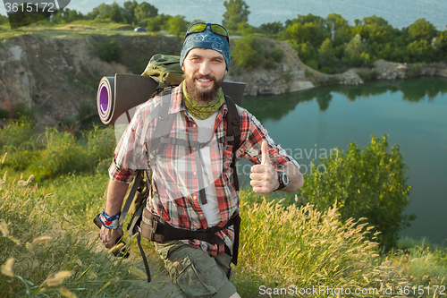 Image of Young caucasian man with backpack walking on the top of hill