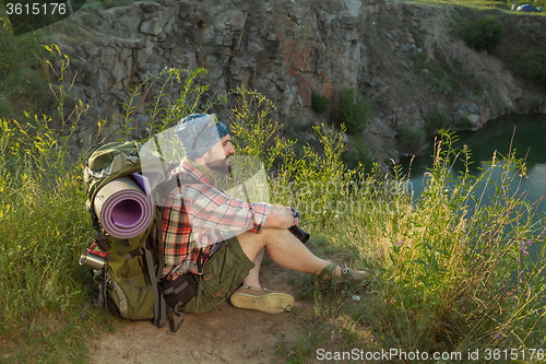 Image of Young caucasian man with backpack sitting on the top of hill