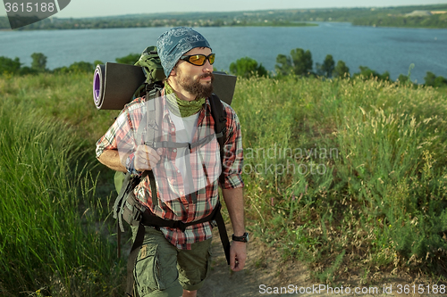 Image of Young caucasian man with backpack walking on the top of hill