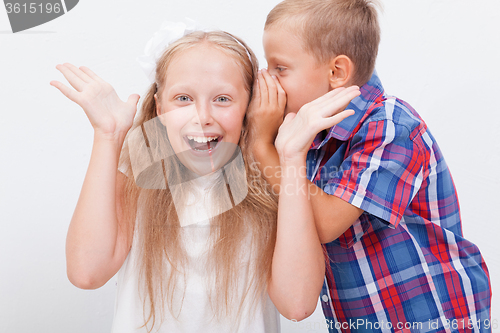 Image of Teenage boy whispering in the ear a secret to teen girl on white  background