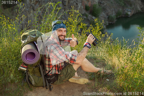 Image of Young caucasian man with backpack sitting on the top of hill