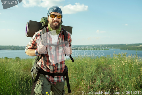 Image of Young caucasian man with backpack walking on the top of hill