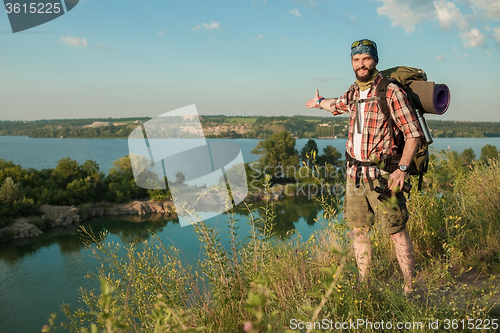 Image of fully equipped tourist smiling on the background of lake