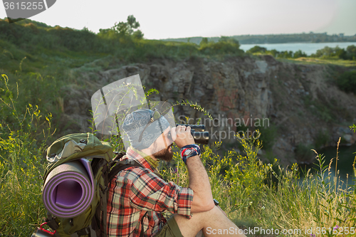 Image of Young caucasian man with backpack sitting on the top of hill