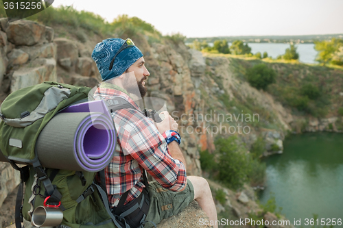 Image of Young caucasian man with backpack sitting on the top of hill
