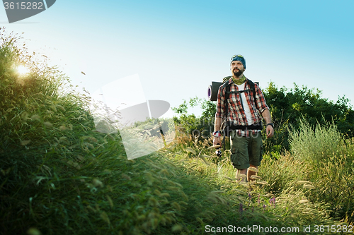 Image of Young caucasian man with backpack walking on a green meadow