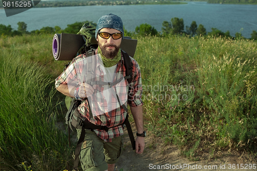 Image of Young caucasian man with backpack walking on the top of hill