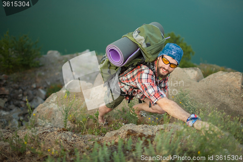 Image of Young caucasian man with backpack rising on the rock