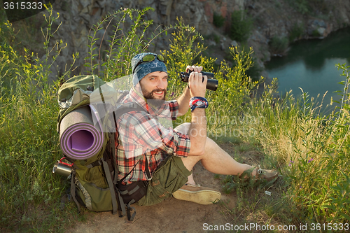 Image of Young caucasian man with backpack sitting on the top of hill