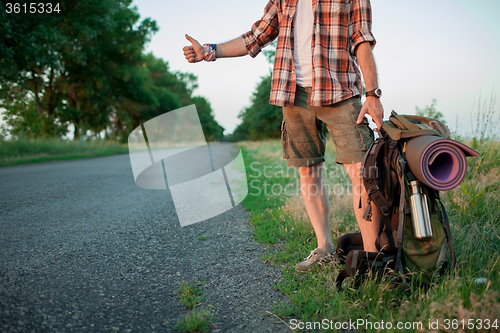 Image of Young smilimg caucasian tourist hitchhiking along a road.