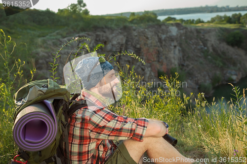 Image of Young caucasian man with backpack sitting on the top of hill