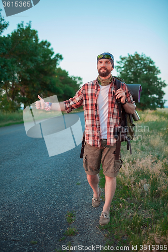 Image of Young smilimg caucasian tourist hitchhiking along a road.