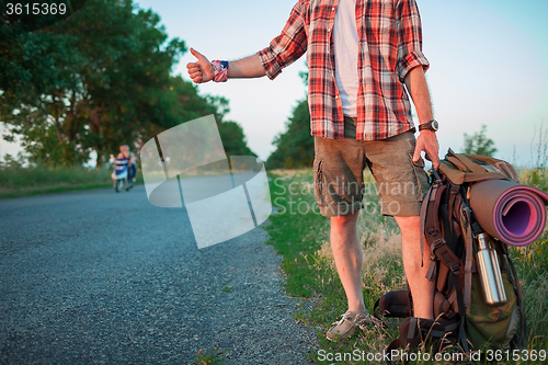 Image of Young caucasian tourist hitchhiking along a road.