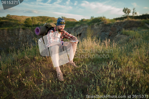 Image of Young caucasian man with backpack sitting on the top of hill