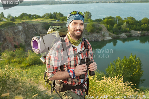 Image of fully equipped tourist smiling on the background of lake