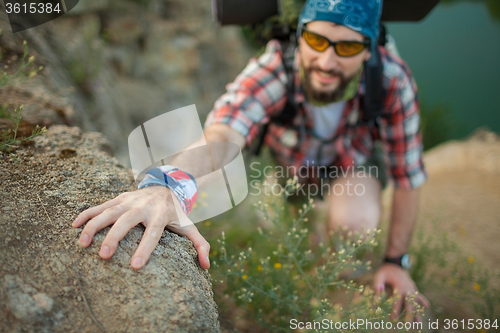 Image of Young caucasian man with backpack rising on the rock