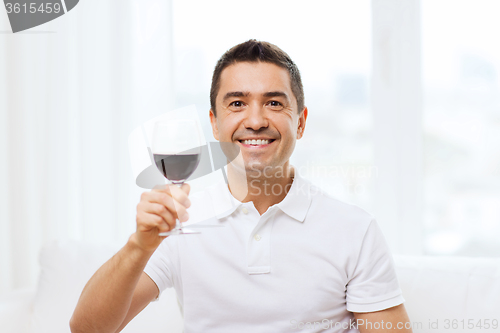 Image of happy man drinking red wine from glass at home