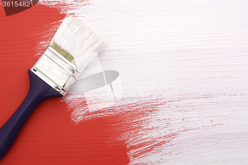Image of Paintbrush with white paint painting over red