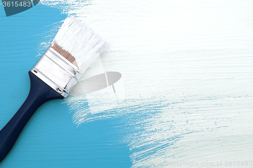 Image of Paintbrush with white paint painting over blue