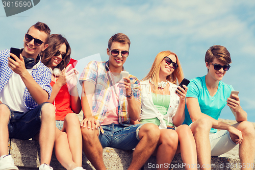 Image of group of smiling friends with smartphones outdoors