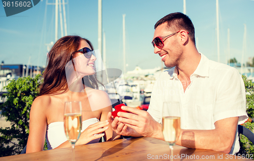 Image of smiling couple with champagne and gift at cafe