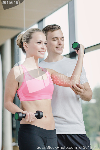 Image of smiling young woman with personal trainer in gym