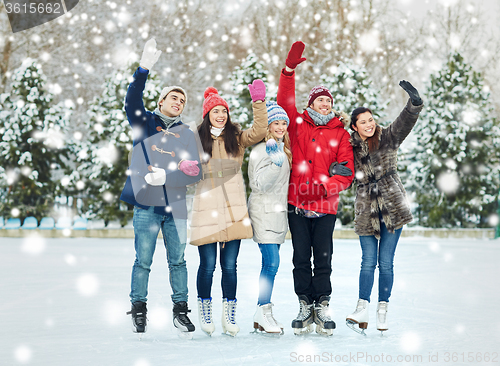 Image of happy friends ice skating on rink outdoors