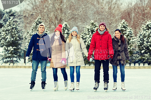 Image of happy friends ice skating on rink outdoors