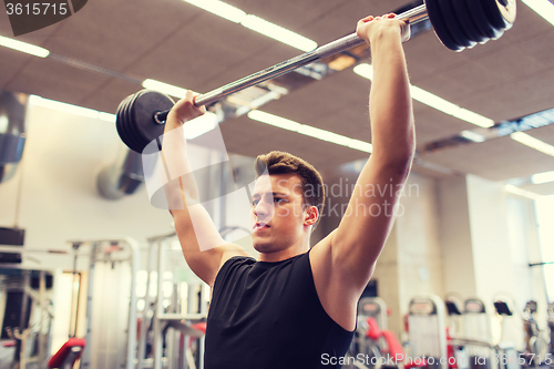 Image of young man flexing muscles with barbell in gym