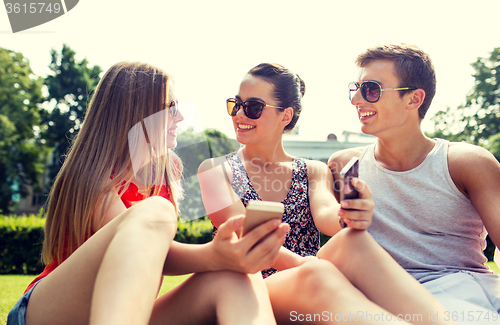 Image of smiling friends with smartphones sitting on grass