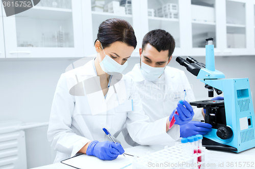 Image of scientists with clipboard and microscope in lab