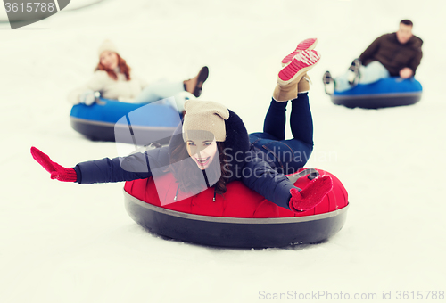 Image of group of happy friends sliding down on snow tubes