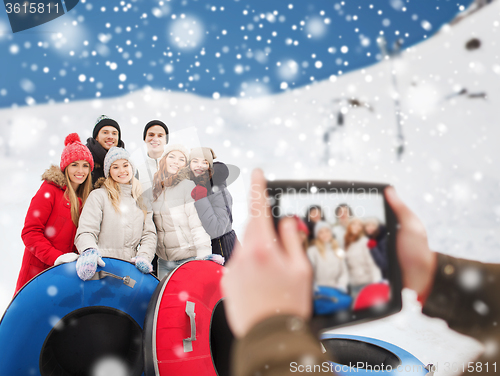 Image of smiling friends with snow tubes and tablet pc