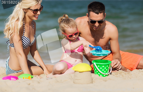 Image of happy family playing with sand toys on beach