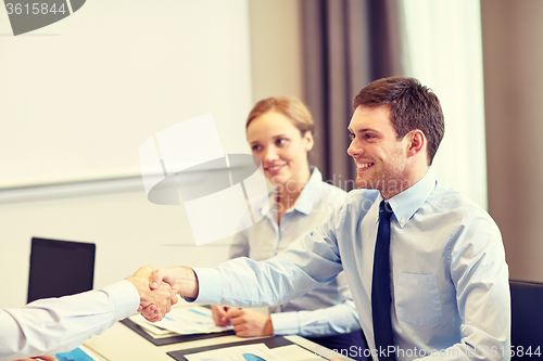 Image of smiling business team shaking hands in office