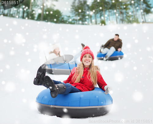 Image of group of happy friends sliding down on snow tubes